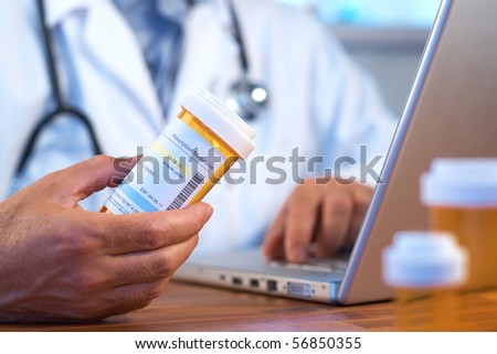Doctor holding prescription bottle with laptop selective focus