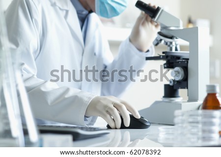 Scientist conducting research looking through microscope with computer selective focus