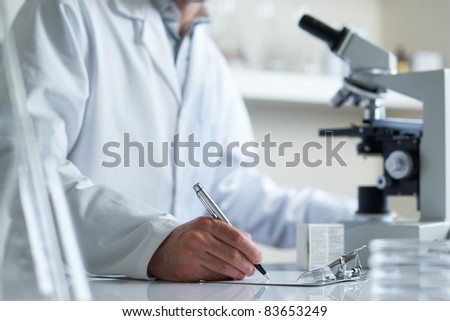 Scientist making notes conducting research looking through microscope selective focus