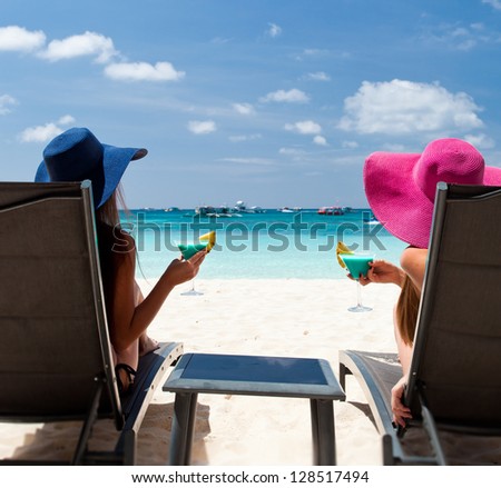 Two ladies in hat sitting in chaise longue with glass of cocktail