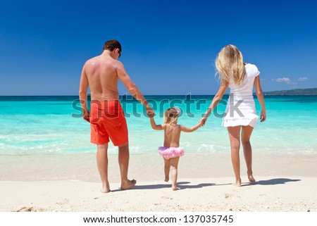 Mother, father and daughter having fun on tropical white beach