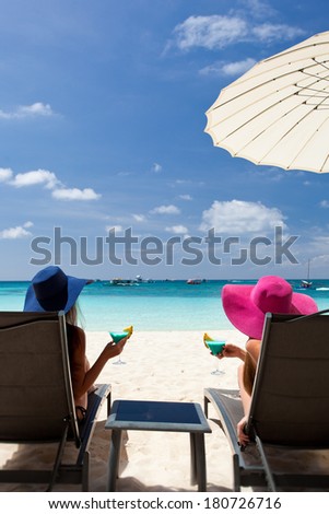 Two ladies in hat sitting in chaise longue with glass of cocktail