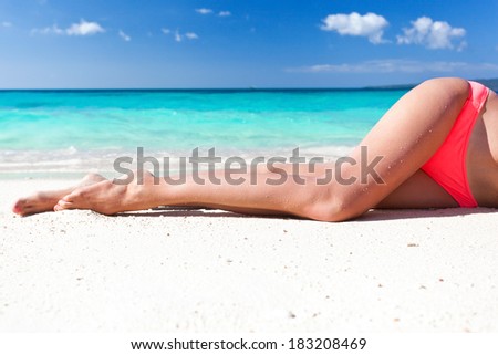Tan slim legs lying on white sandy beach near sea, no face