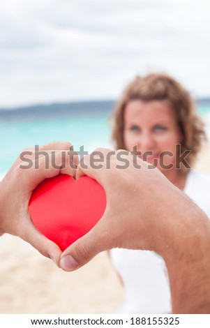 Loving couple on beach, red heart in hand