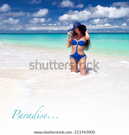 Beautiful tan woman in blue summer hat posing on tropical beach. Happy vacation