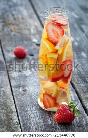 Bottle with sliced oranges and strawberries on wooden table, organic vegan drink.Focus on bottle