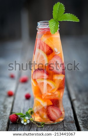 Bottle with sliced oranges and strawberries on wooden table, organic vegan drink