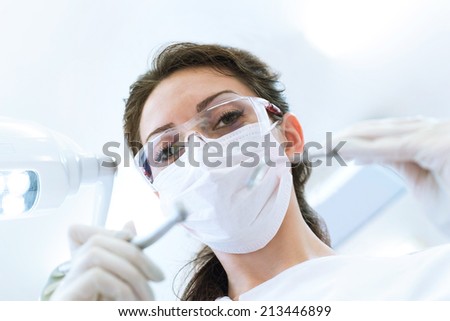 Dentist wearing surgical mask while holding angled mirror and drill, ready to begin