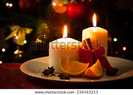 Christmas decoration, candles, cinnamon sticks and pieces of orange, on christmas tree background