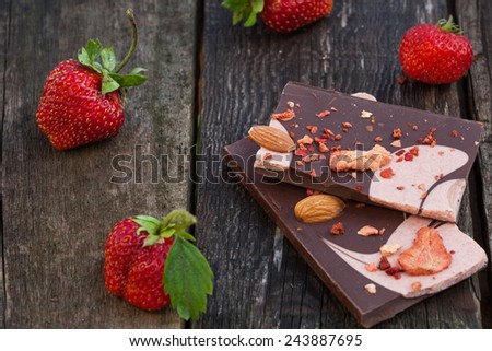 Handmade dark chocolate bar with strawberry slices closeup to fresh berries on old wooden table
