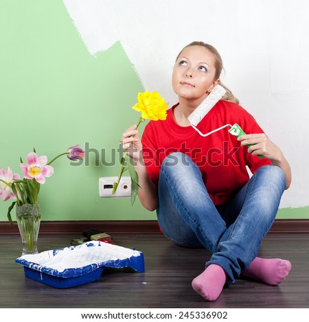 Young woman with flower and paint roller in hands painting interior wall of home