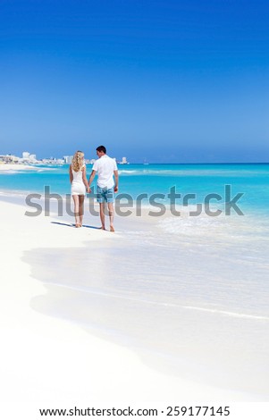 Romantic couple walking on perfect beach with turquoise sea, enjoying life and each other at honeymoon vacation. Back view