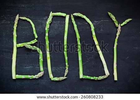 Word Body made of asparagus vegetables on black wooden board. Top view. Healthy food concept.