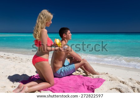 Woman applying heart shape sun protection lotion on man back, summer tropical beach vacation