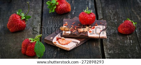 Handmade dark chocolate bar with strawberry slices closeup to fresh berries on old wooden table