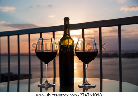 Silhouette of bottle and glasses with red wine in sunset with sea view background
