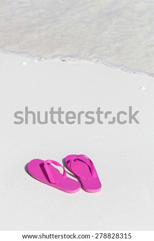 Pink flip flops on white sandy beach near sea waves, nobody. Summer vacation concept
