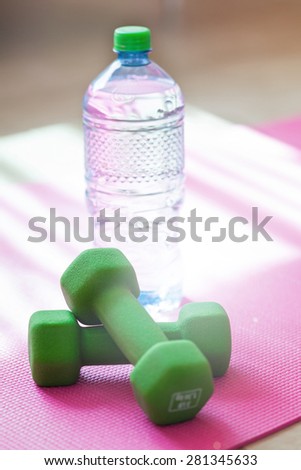 Two dumbbells with mineral water on yoga mat against the sunlight, shallow depth. It\'s very important to drink water at workout training. Sporty lifestyle concept without dehydration.