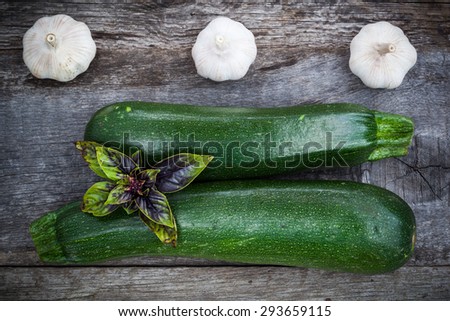 Fresh green zuchinni with basil leaves and garlic on wooden board, top view, focus on garlic