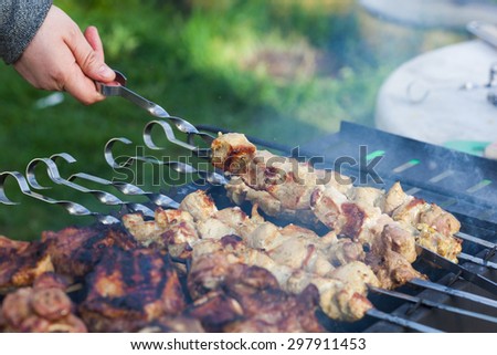Cooking lamb steaks and pork kebab on grill, skewered pork meat in hand, outdoor. Selective focus and shallow DOF