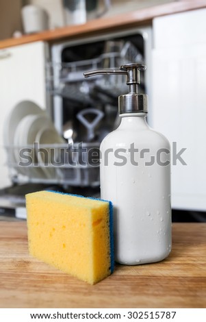 Dishwasher sponge with soap in dispenser tube on background of opened dishwasher machine after cleaning process. Technology timesaving concept.
