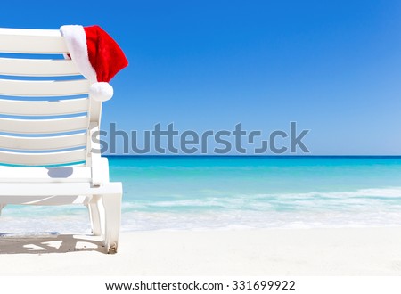 Santa Claus Hat on sunbed near  tropical calm beach with turquoise caribbean sea water and white sand. Christmas vacation concept