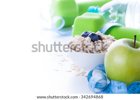 Fitness frame with energy breakfast, oatmeal, apple and mineral water with sport tools on background. Healthy weight loss concept with copy space.
