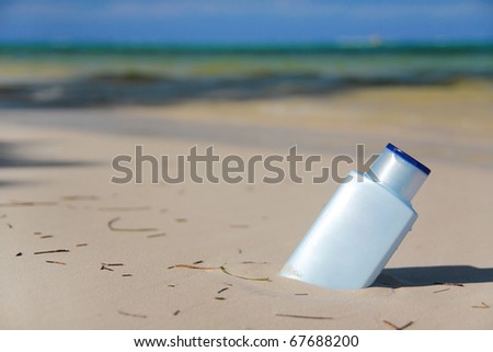Blue bottle with Sunblock lotion in sand on tropical beach, outdoor
