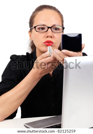 Businesswoman in black office blouse with spectacles looking to mirror using red lipstick