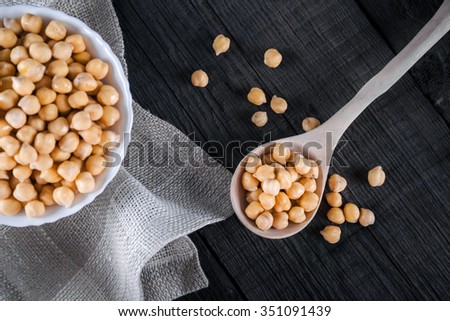 Steamed gold chickpeas in bowl on tablecloth with wooden spoon, tasty vegan food, top view, selective focus