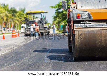 Road construction works with steamroller machine and asphalt finisher