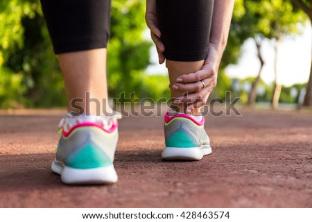 Female athlete runner touching foot in pain,closeup, fitness woman running in summer park. Healthy lifestyle and sport concept
