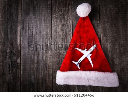 White blank toy of passenger plane on Santa Claus helper hat on rustic wooden background. Christmas and New Year celebration