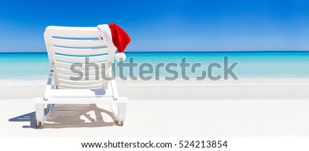 Santa Claus Hat on sunbed near tropical calm beach with turquoise caribbean sea water and white sand. Christmas vacation celebration