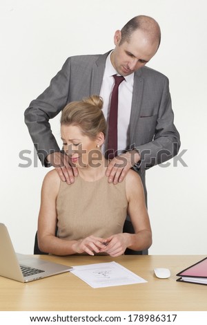 Harassment in the workplace as a randy male boss stands behind a female colleague groping her shoulders with his hands