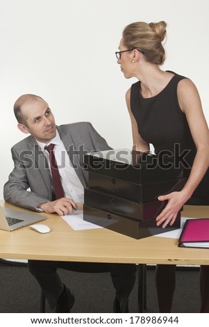 Image of a male boss giving dirty looks to the female assistant, while she\'s putting a bunch of folders on his table, office politics.