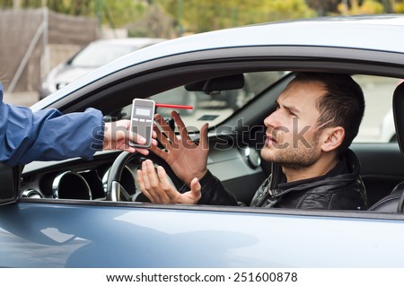 Young driver arguing with a police officer during test for alcohol content with breathalyzer, he is angry and not willing to participate with police officer