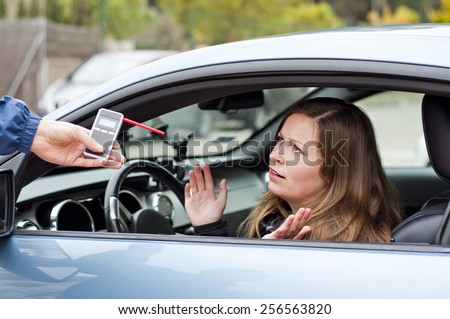 Young female driver arguing with a police officer during test for alcohol content with breathalyzer, she is angry and not willing to cooperate with police officer