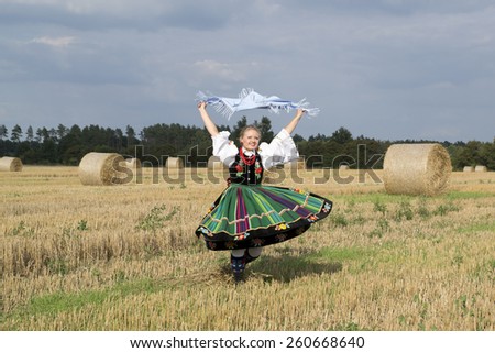 Blonde pretty young smiling girl dressed in Polish national folk dress dancing and spinning around  in the field of harvest straw bales