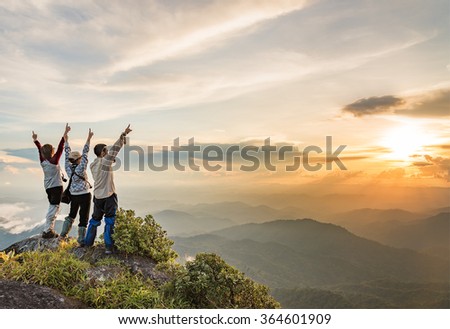 Happy people on top of a mountain enjoying valley view while the sun is setting.