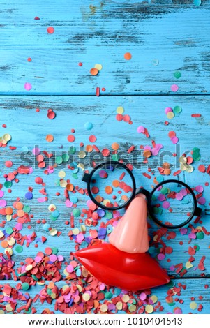 high angle view of a pair of fake black glasses, a nose and a mouth forming the face of a person on a blue rustic wooden surface full of confetti