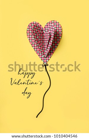 high angle shot of some colorful cutout hearts and a string drawn simulating a balloon, and the text happy valentines day on a yellow background