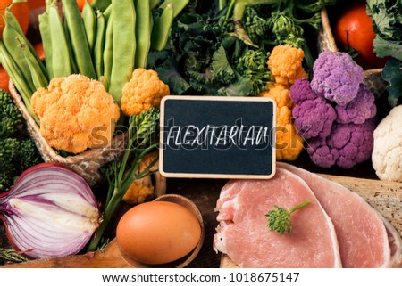 closeup of a signboard with the text flexitarian on a pile of some different raw vegetables, such as cauliflower of different colors, broccolini, or french beans, and some eggs and slices of meat