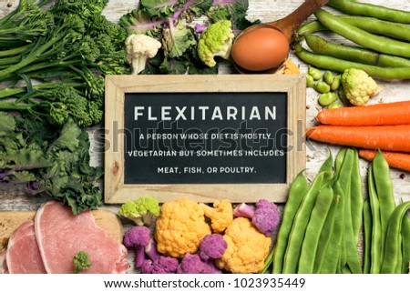 a signboard with the text flexitarian and its definition on a pile of some different raw vegetables, such as cauliflower of different colors, broccolini, beans, and some eggs and slices of meat