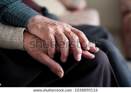 closeup of an old caucasian man and an old caucasian woman sitting in a couch holding hands with affection