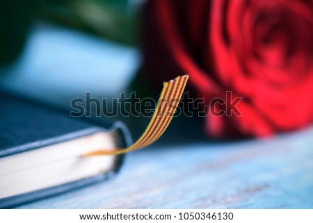 a red rose and a catalan flag on a book, on a blue table, for Sant Jordi, the Catalan name for Saint Georges Day, when it is tradition to give red roses and books in Catalonia, Spain