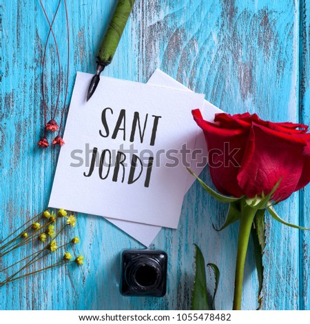 high angle view of a red rose, an ink bottle, a nib pen and the text Sant Jordi, the name of Saint George Day in Catalan, when it is tradition to give red roses and books in Catalonia, Spain