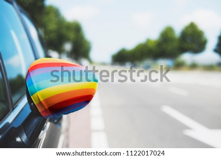 closeup of a rainbow flag in the wing mirror of a car