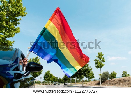 closeup of a young caucasian man waving a rainbow flag by the window of a car