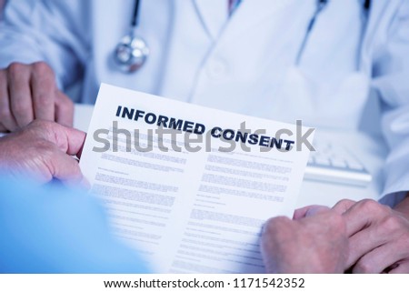 closeup of a senior caucasian man, at the doctors office, reading an informed consent document in front of a caucasian doctor man, in a white coat, sitting both at the doctors desk